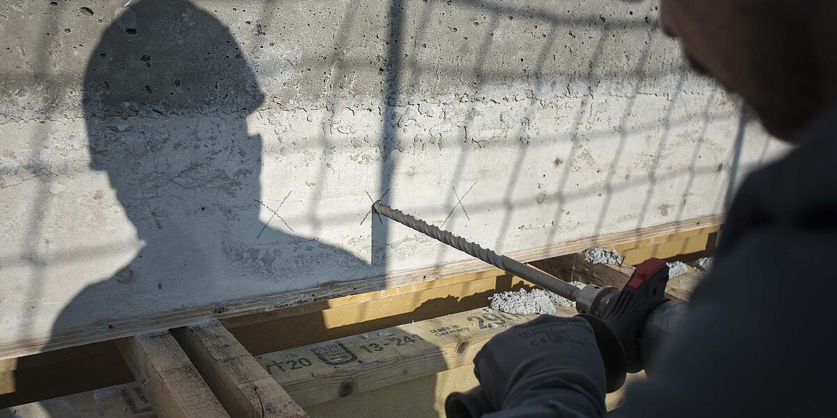 Mann bohrt in eine Betonwand